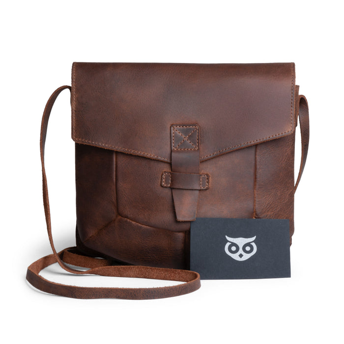 The Prisma Shoulder Bag from Hide & Drink with a business card alongside it, demonstrating its practicality and style. This vintage purse serves as a beautiful messenger and crossbody bag made from full grain leather, reflecting the small batch artisan production from La Antigua Guatemala & Oaxaca Mexico.