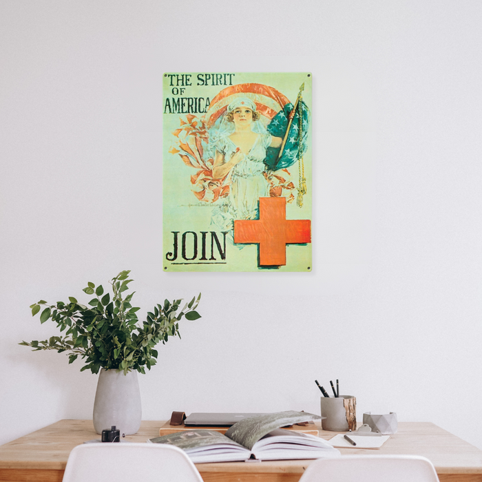 Vintage recruitment poster hangs on a white wall above a wooden desk featuring a woman holding a flag, with the text The Spirit of America. There is a Red Cross symbol with the text Join written below. Designed in the iconic style of Howard Chandler Christy.