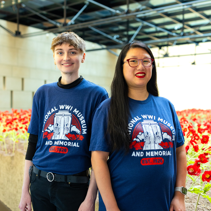 Two people wearing a dark blue t-shirt that depicts the Liberty Memorial Tower with poppy flowers. Arching over the tower is the text 'National WWI Museum and Memorial'. There are poppy flowers in the background.
