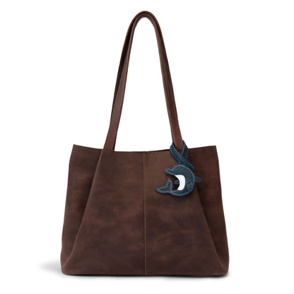 Hide & Drink Bag Charms attached to a trendy brown handbag, showcasing a playful monster design perfect for personalization. This accessory serves as a purse charm for tote & backpacks made from durable full grain leather, highlighting StockyardX's dedication to small batch production. Each piece features hand cut, hand sewn artistry along with fire branding, handmade in La Antigua Guatemala & Oaxaca Mexico.