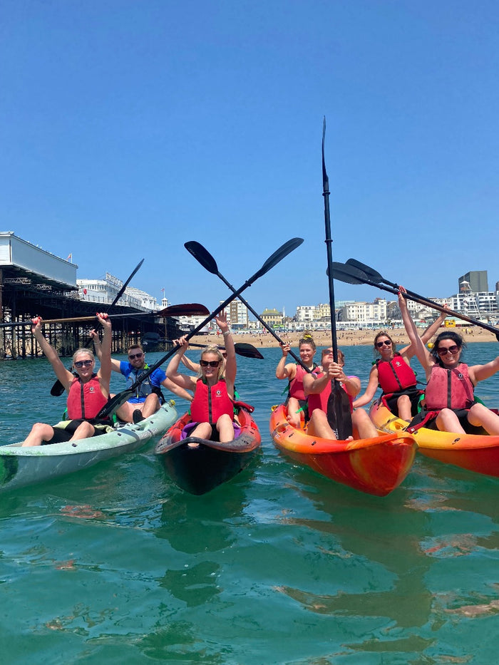 Kayak group on Brighton sea with paddles in air