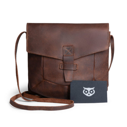The Prisma Shoulder Bag from Hide & Drink with a business card alongside it, demonstrating its practicality and style. This vintage purse serves as a beautiful messenger and crossbody bag made from full grain leather, reflecting the small batch artisan production from La Antigua Guatemala & Oaxaca Mexico.